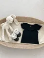 Flat lay of baby girl flutter sleeve top with ruffle collar and lace socks in a cradle - 66 / Black