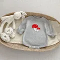 Dettaglio tutina neonato in maglia grigia con ricamo a fungo in un cesto di vimini - 66CM / Grigio