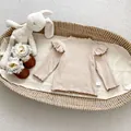 Detailaufnahme des gerippten Langarm-Babytops und kaffeebraunen Weichschuhen in der Wiege - Größe 73 / Khaki Unterziehshirt