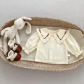 Detailansicht der Babybluse mit Spitzenkragen, roter Stickerei und weißen Knöpfen - 66cm / Beiges Besticktes Hemd