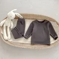 Flat lay of charcoal gray thermal baby pajamas set in a woven basket with a soft toy - Dark Gray