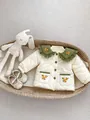 Detail der gesteppten Babyjacke mit grünem besticktem Kragen im Weidenkorb - Aprikose / 66CM