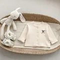 Detail van gebreid babyvestje met houten knopen en geborduurde strik in een geweven mand - 66cm / Abrikoos Top