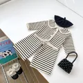 Gedetailleerde flat lay van gestreepte gebreide peuterset met vest en chique accessoires - Gestreept / 73cm