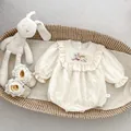 Creamy white baby romper with floral embroidery and ruffle collar in a woven basket - 66cm / Apricot
