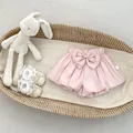 Close-up of pink baby bloomers with a large bow detail and a white size 73 tag - Pink