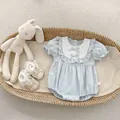 Detail of light blue baby romper with bow accents and ruffles in a cozy woven basket - 66 / Blue