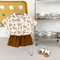 Dettaglio camicia estiva in cotone per neonato con stampa cane e pantaloncini marroni su gruccia - Stampa Cane Bianco Sporco / 73cm