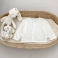 Close-up van de ribtextuur en knopen op een wit babyvestje met maatlabel 73 erop - Wit / 73cm