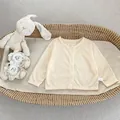 Detailopname van crème gebreid vestje voor peuters met gele strik in een geweven mand - 73cm / Abrikoos