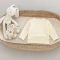 Detail of baby beige knit top with ruffle edges and size label in a woven basket - 66 / Apricot