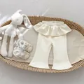 Detalle de pantalones con volantes blanco roto y zapatos de bebé en una cesta tejida - 73cm / Albaricoque