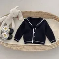 Detail van donkerblauw gebreid babyvest met witte kraag en knopen in een mandje - 73cm / Marineblauw