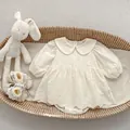 Flat lay of embroidered baby romper dress with matching shoes and plush rabbit toy - Apricot / 66cm