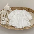Detailed view of white floral embroidery and lace collar on infant cotton romper suit - White / 66cm