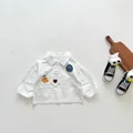 Détail d'une chemise bébé en coton blanc avec broderie ours et badge décoratif sur la poitrine - Chemise Blanche / 73cm