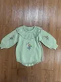Light green baby knit romper with ruffle collar and floral embroidery on a wood surface - Green