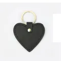 Detail of a black heart-shaped PU leather keychain with cross pattern and gold metal ring - Black