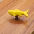 Close-up of a yellow fish-shaped ceramic drawer knob with silver base on wood - Yellow