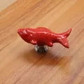 Detail of a bright red fish-shaped ceramic cabinet handle with a silver metal base - Red