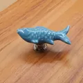Detail of a light blue fish-shaped ceramic cabinet handle with a silver metal base - Blue