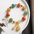 Detailed shot of multi-color pumpkin bead bracelet with jade gourd charm on ceramic tray - Pumpkin Bead Bell With Gourd