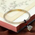 Translucent chalcedony bangle with a red bead and green bell charm on a vintage book - Greyish Brown with Lotus Charm