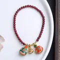 Detalle de pulsera de granate con cascabeles de esmalte de colores y amuleto dorado en plato - Círculo Único Granate Familia de Bestias de la Fortuna