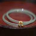 Macro shot of green chalcedony bangle with S925 gold-plated ruyi lock and bells - Apple Green Ruyi Small Bell Pair