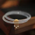 Brazaletes de ágata translúcida con dije de loto dorado y perlas sobre fondo de madera - Blanco