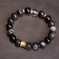 Pulsera de obsidiana plateada con cuentas doradas y cristal sobre fondo de madera - Obsidiana Plateada Cristal Blanco
