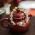 Natural jade bead bracelet with gold lotus charms draped on a classic teapot - Hetian Jade Hand Plate Flower Petal Style