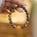 Bracciale in legno di agar con grande perla d'ambra arancione e accenti verdi sulla mano - Stile Ambra Gialla