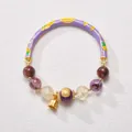 Macro detail of natural amethyst beads with purple enamel metal tube and gold bell charm - Purple Nine Purple Fire Style