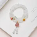Three-wrap natural jade beaded bracelet with floral pendant on a book background - Tianshan Jade Fluorite Lion