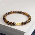 Brown tiger eye bead bracelet with a matte gold fish charm on a white book - 6mm / Yellow Tiger Eye Koi Style