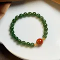 Detailed shot of jasper beaded bracelet with red agate accent on white ceramic tray - 8mm Green Jade Southern Red Agate Gold Plated Silver Bracelet