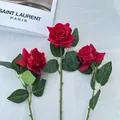 Three realistic red artificial roses with green leaves on white textured fabric - Red