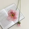 Rosa künstliche Mohnblume aus Seide mit grünem Stiel auf einem offenen Buch - Rosa