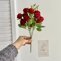 Single hand holding a bouquet of ten deep red artificial roses with green silk leaves - Red