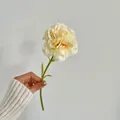 Single pale yellow carnation artificial flower with soft pink edges held by hand - Champagne