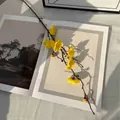 Rama de flor de ciruelo artificial amarilla con núcleo rojo sobre una revista - Ruyi Flor de Ciruelo Amarillo