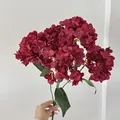 Handheld dark red artificial hydrangea bunch with dense petals and realistic green leaves - Red