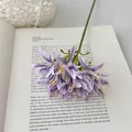 Τεχνητή μωβ ανθοδέσμη Agapanthus από μετάξι πάνω σε ένα ανοιχτό βιβλίο διακόσμησης - Μωβ