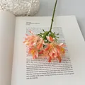 Artificial orange lily bouquet with lifelike green stems on an open book background - Orange