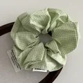 Macro view of green gingham check fabric scrunchie with woven label on wooden tray - Green