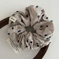 Macro view of beige scrunchie with colorful embroidered dots and brand label detail - Apricot