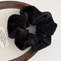 Minimalist black corduroy scrunchie with a velvet-like texture on a rustic wooden display - Black