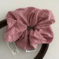 Detail of red and white gingham scrunchie with brand label on a wooden display - Red