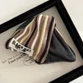 Detail of striped knit hair claw featuring a Black Cat logo label and premium fabric texture - Khaki Brown